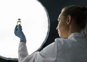 Scientist examining a vial under laboratory lighting, wearing protective gloves and a lab coat