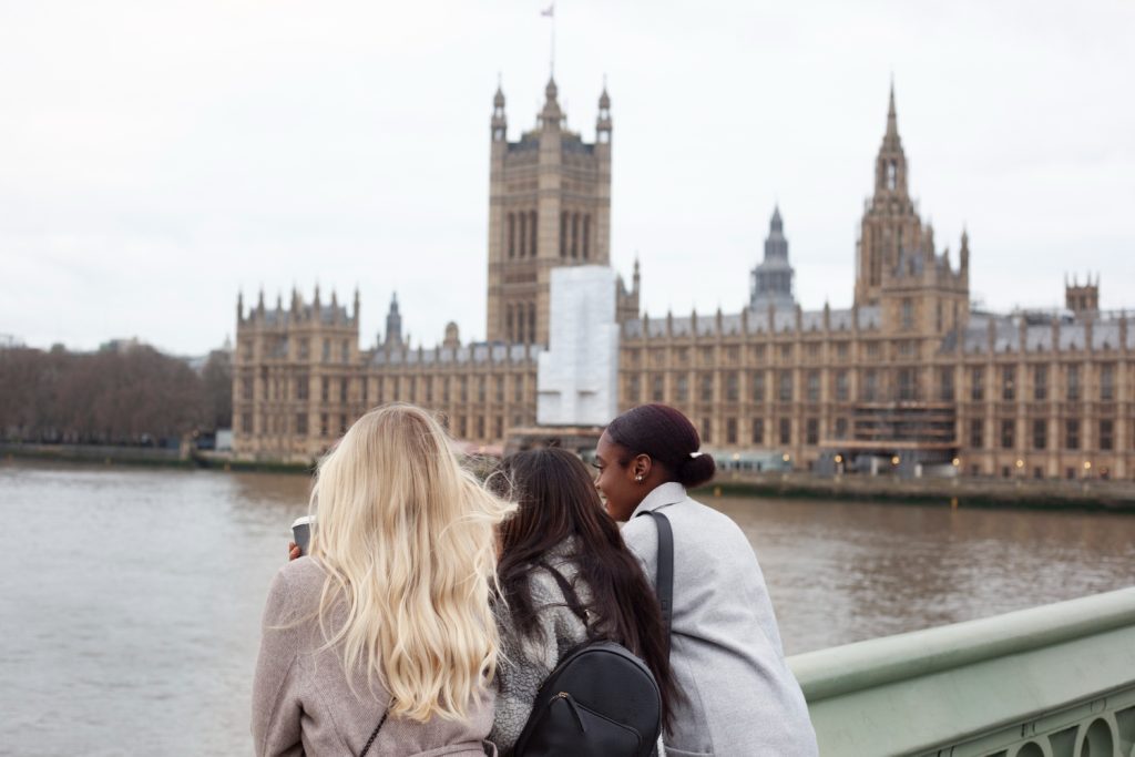 Three women admire the Houses of Parliament from across the River Thames in London