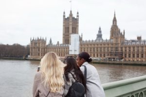 Three women admire the Houses of Parliament from across the River Thames in London