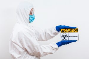 A man in a white hazmat suit holds a caution sign, indicating a hazardous area or situation