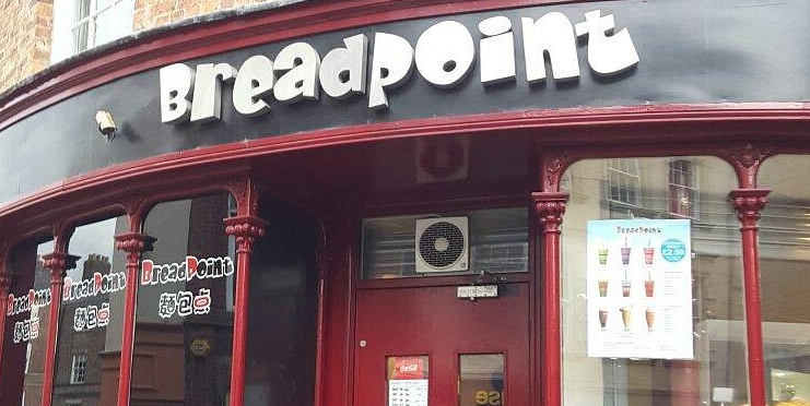 Breadpoint bakery storefront with red columns and a menu display in the window