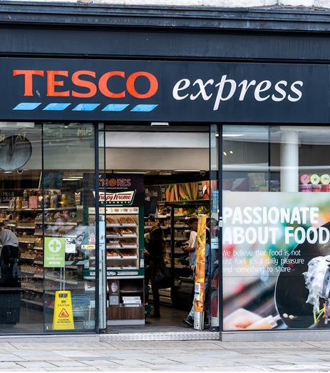 Tesco Express storefront with signage, glass windows displaying products, and a poster about passion for food