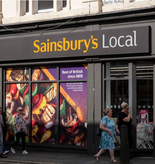 People walking past a Sainsbury's Local store with colourful window display in the UK