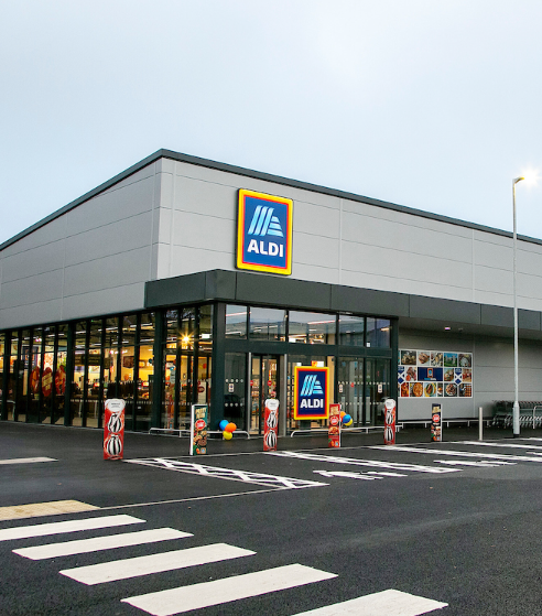Exterior view of an ALDI supermarket with parking and signage, featuring modern architecture and a welcoming entrance