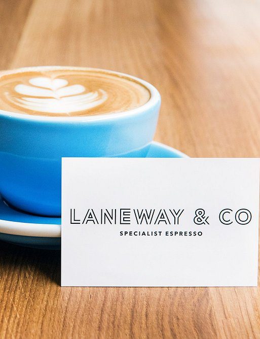 Blue coffee cup with latte art next to Laneway & Co business card on wooden table