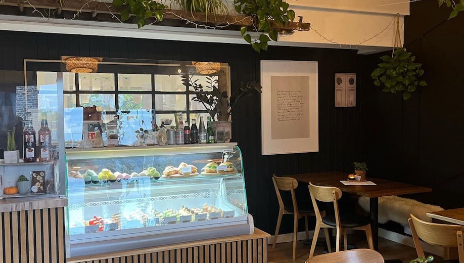 Cosy café interior with display of pastries and drinks, wooden chairs and green plants creating a welcoming atmosphere
