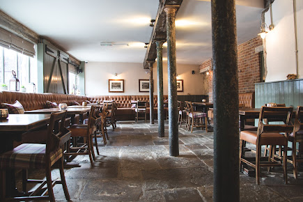 Rustic pub interior with wooden beams, cushioned seating, and stone floors creating a cosy dining atmosphere