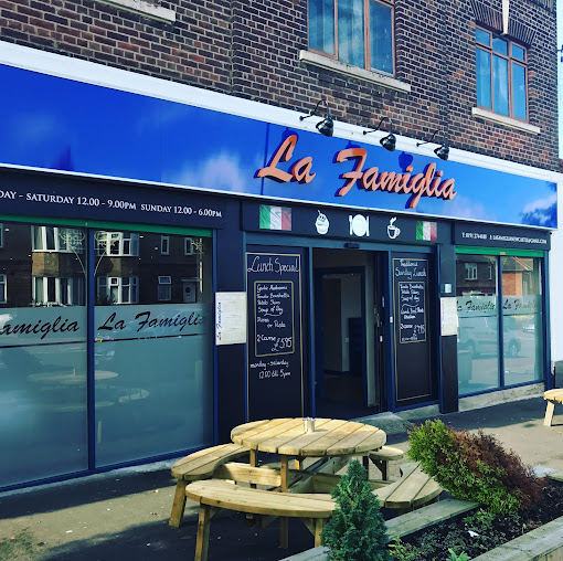 Outside view of La Famiglia restaurant with blue signage, outdoor seating and menu boards in the forefront