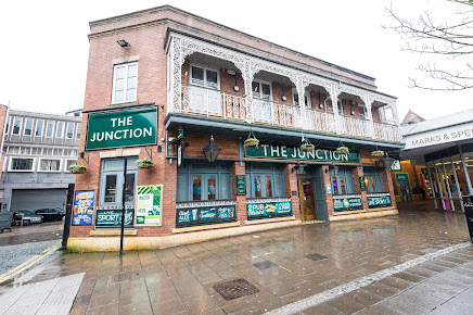 The Junction pub exterior on a rainy day with decorative balcony, located next to Marks & Spencer in a shopping area