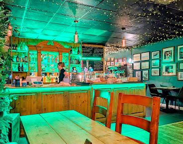 Cosy bar interior with wooden counter, vibrant green lighting, and decorative wall art creating a welcoming ambience