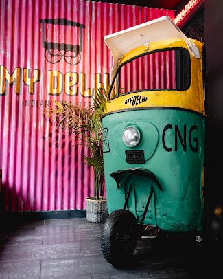Retro green and yellow rickshaw with 'CNG' signage inside an Indian restaurant with pink corrugated walls