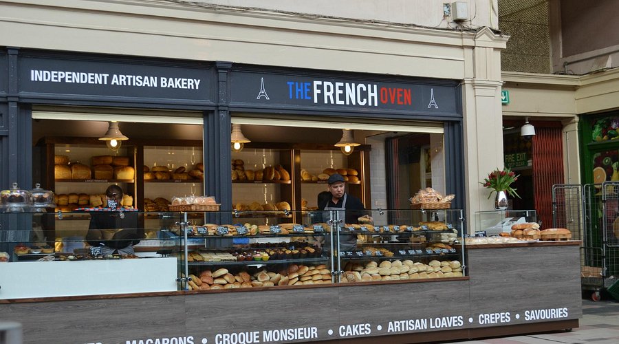Independent artisan bakery storefront displaying a variety of breads and pastries at The French Oven in a marketplace setting
