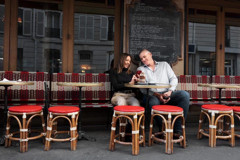 A man and woman seated at a table outside a restaurant, enjoying a meal together