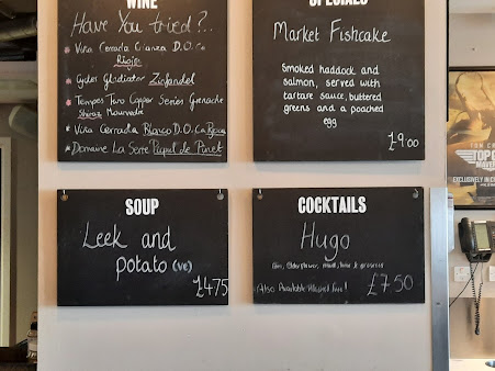 Restaurant menu board featuring wine, soup, fishcake, and cocktail options with prices displayed